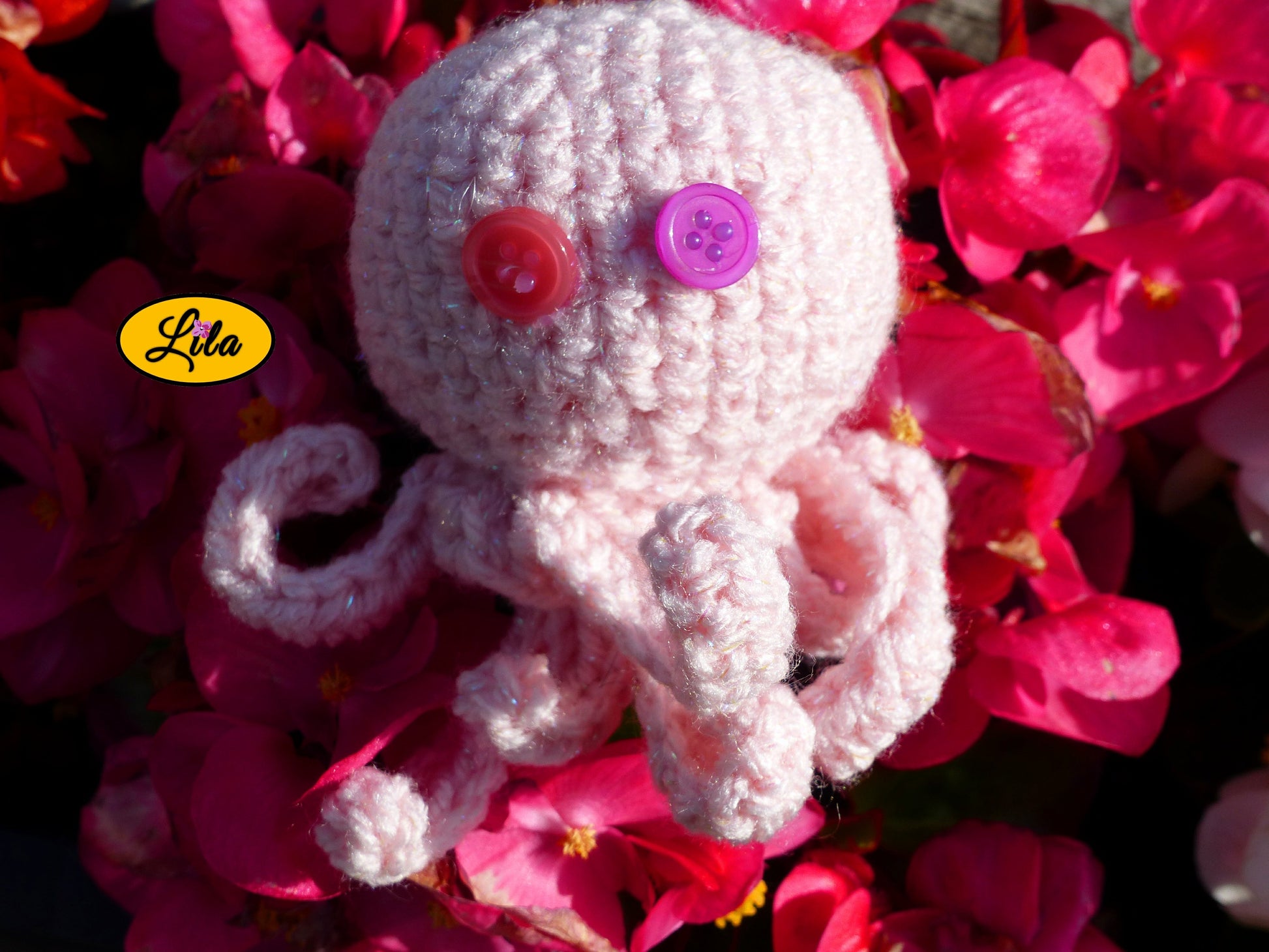 Porte-clé Poulpy pieuvre amigurumi rose clair réalisée au crochet avec yeux en boutons rose et mauve posé sur un lit de fleurs roses style kawaii et artisanal