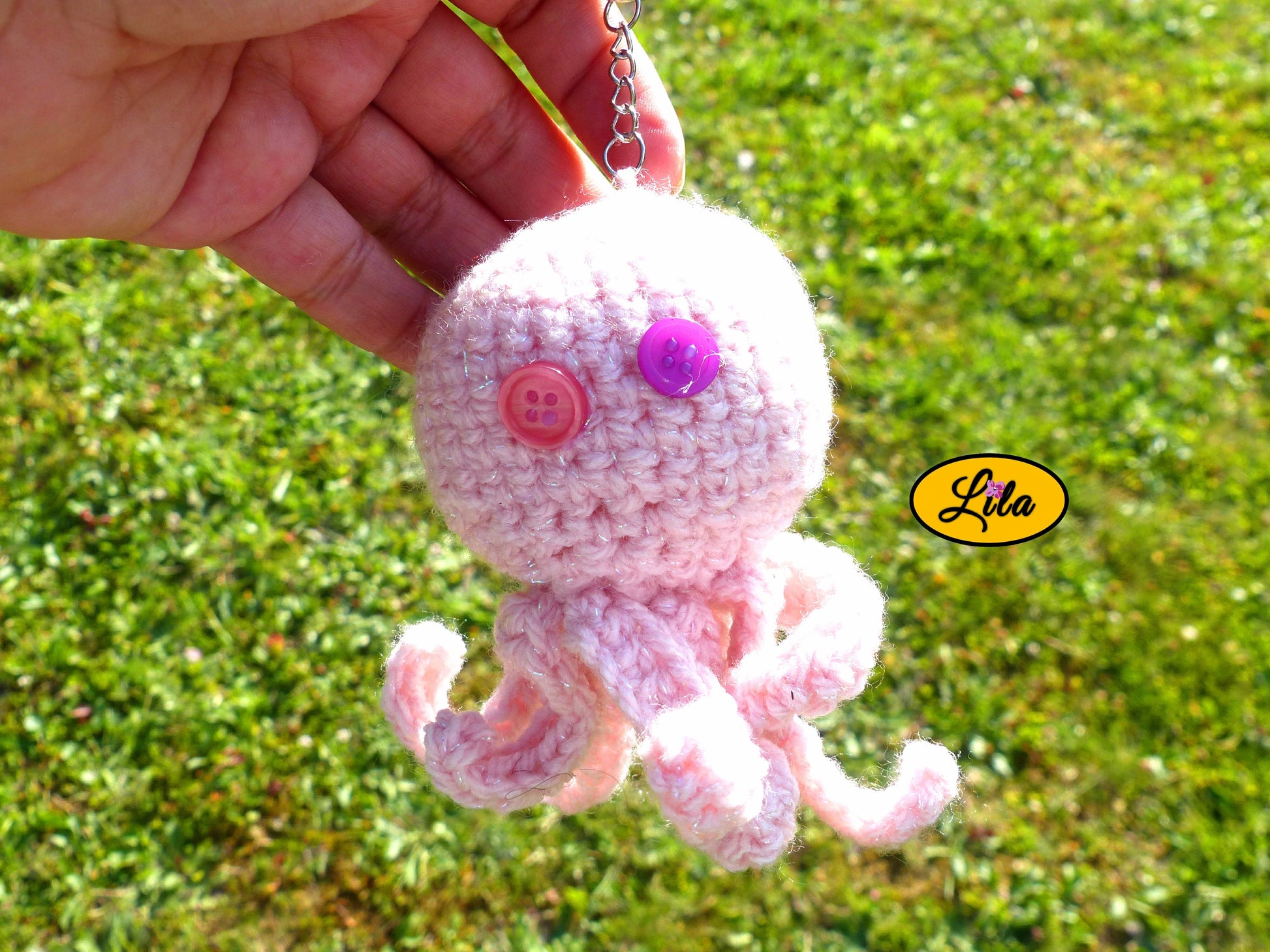 Porte-clé Poulpy pieuvre amigurumi rose clair réalisée au crochet avec yeux en boutons rose et mauve tenu dans une main en extérieur dans un jardin style handmade et kawaii
