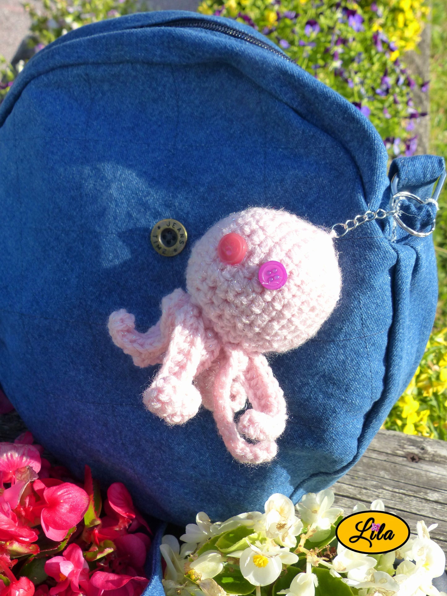 Porte-clé Poulpy pieuvre amigurumi rose clair au crochet avec yeux en boutons rose et mauve accroché à un sac en jeans près de fleurs style bohème et artisanal