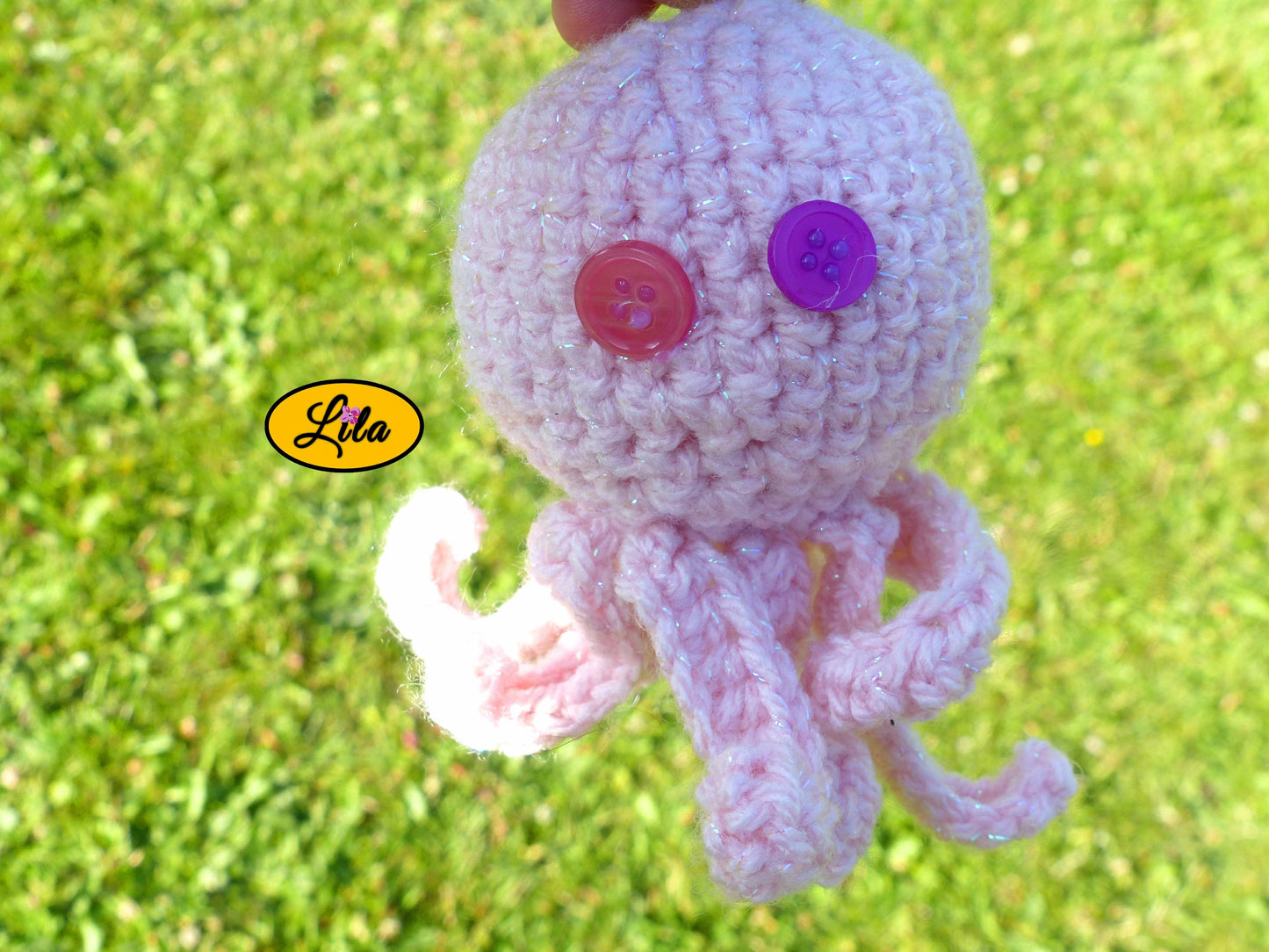 Porte-clé Poulpy pieuvre amigurumi rose clair réalisée au crochet photographié sous un autre angle dans un jardin avec yeux en boutons dépareillés rose et mauve style kawaii et bohème