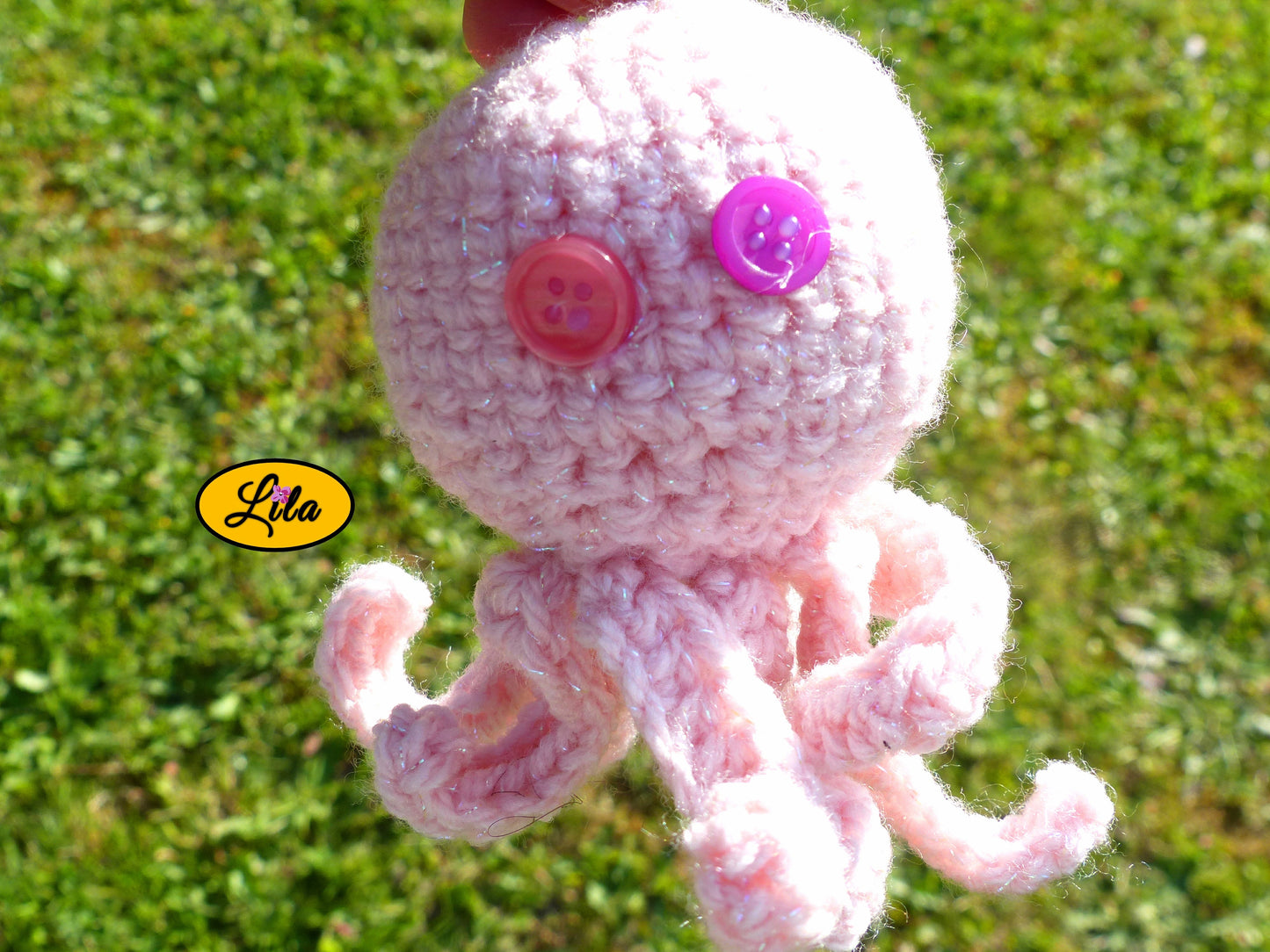 Photo rapprochée du porte-clé Poulpy pieuvre amigurumi rose clair au crochet avec yeux en boutons rose et mauve dans un jardin style artisanal et mignon