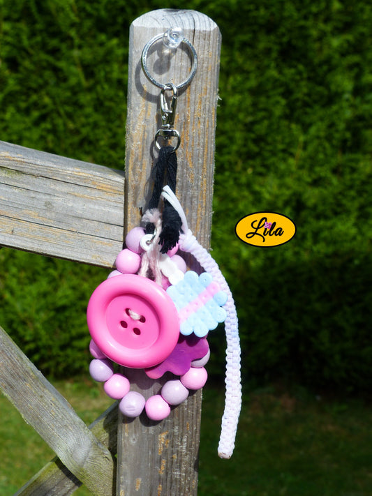 Porte-clés rose sucrée rétro chic composé d’une sucette pastel en perles à repasser, fleur en pâte polymère rose dégradé, bracelet en grosses perles mauves et roses pastel, scoubidou pastel, gros bouton rose et bouts de laine tressée suspendus à un mousqueton style kawaii et artisanal