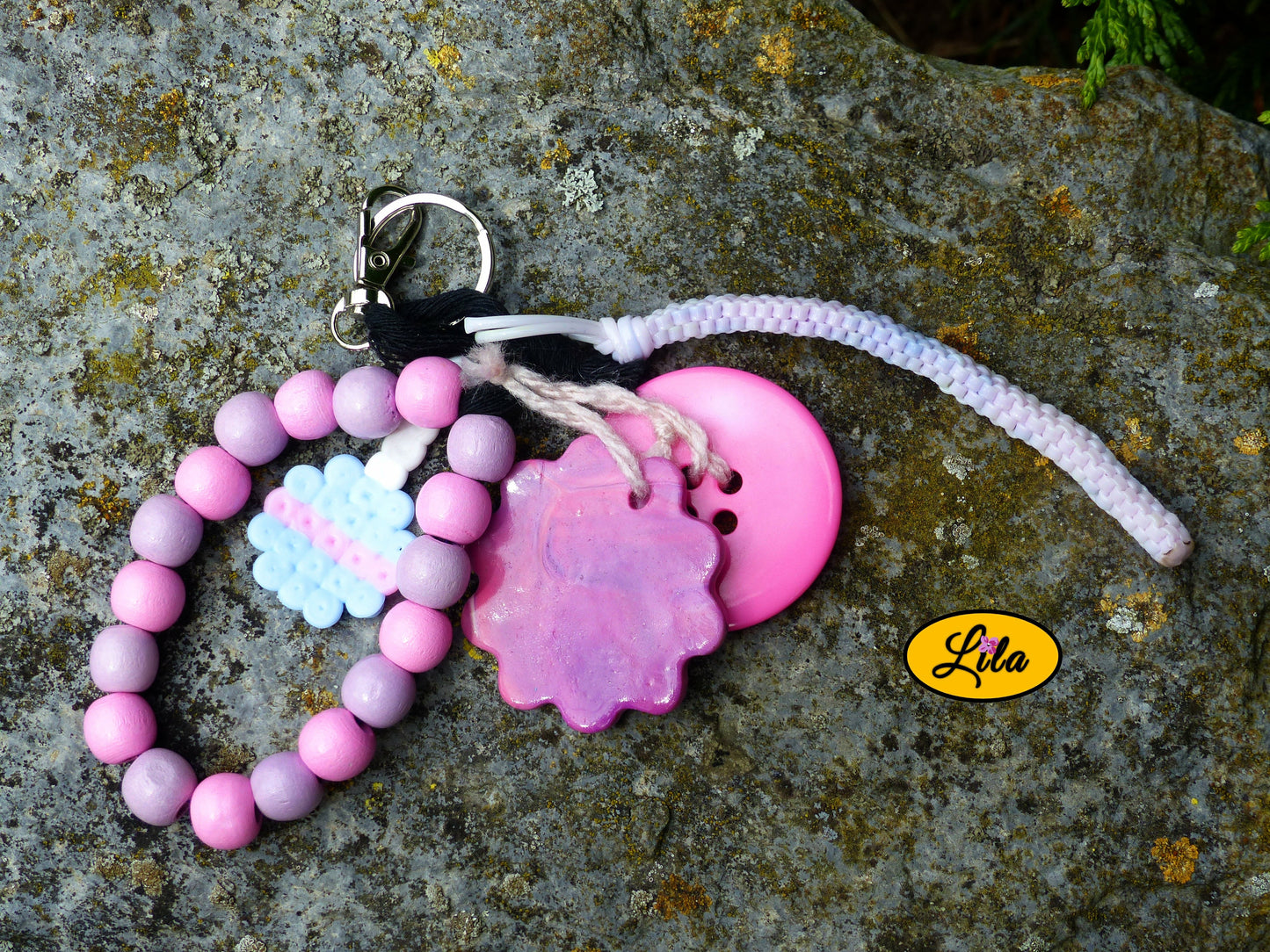 Porte-clés rose sucrée rétro chic posé sur une pierre vue de haut avec sucette pastel en perles à repasser, fleur en pâte polymère dégradée, grosses perles roses et mauves, bouton rose et scoubidou pastel visibles côte à côte style créatif et bohème