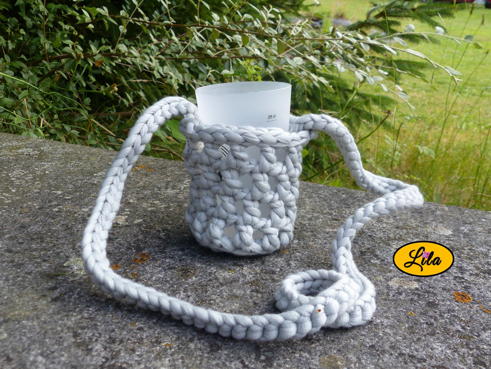 Porte-gobelet gris avec tresse pour port autour du cou façon collier pendant et gobelet à l’intérieur posé de face sur une pierre en extérieur style festival et artisanal