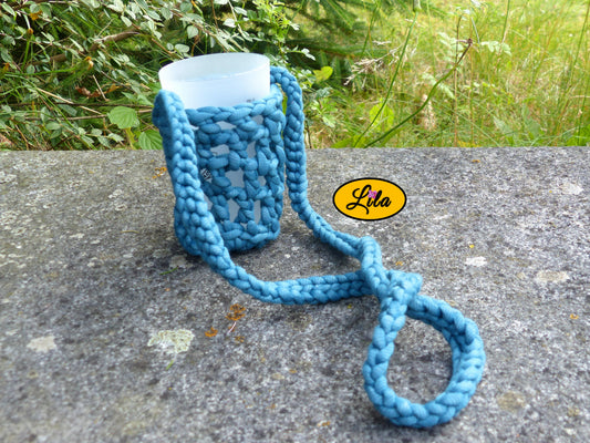 Porte-gobelet turquoise avec tresse pour port autour du cou façon collier pendant et gobelet à l’intérieur posé de face sur une pierre en extérieur style festival et artisanal
