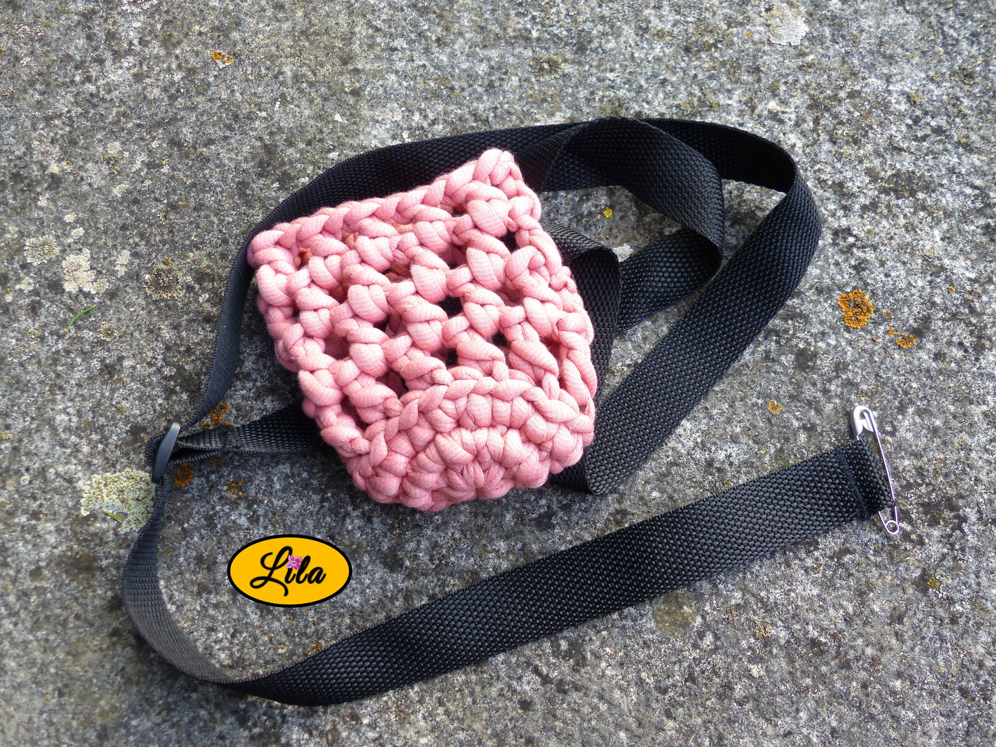 Porte-gobelet crocheté rose vu de haut avec ceinture noire entourant le porte-gobelet posé sur une pierre style bohème et festival