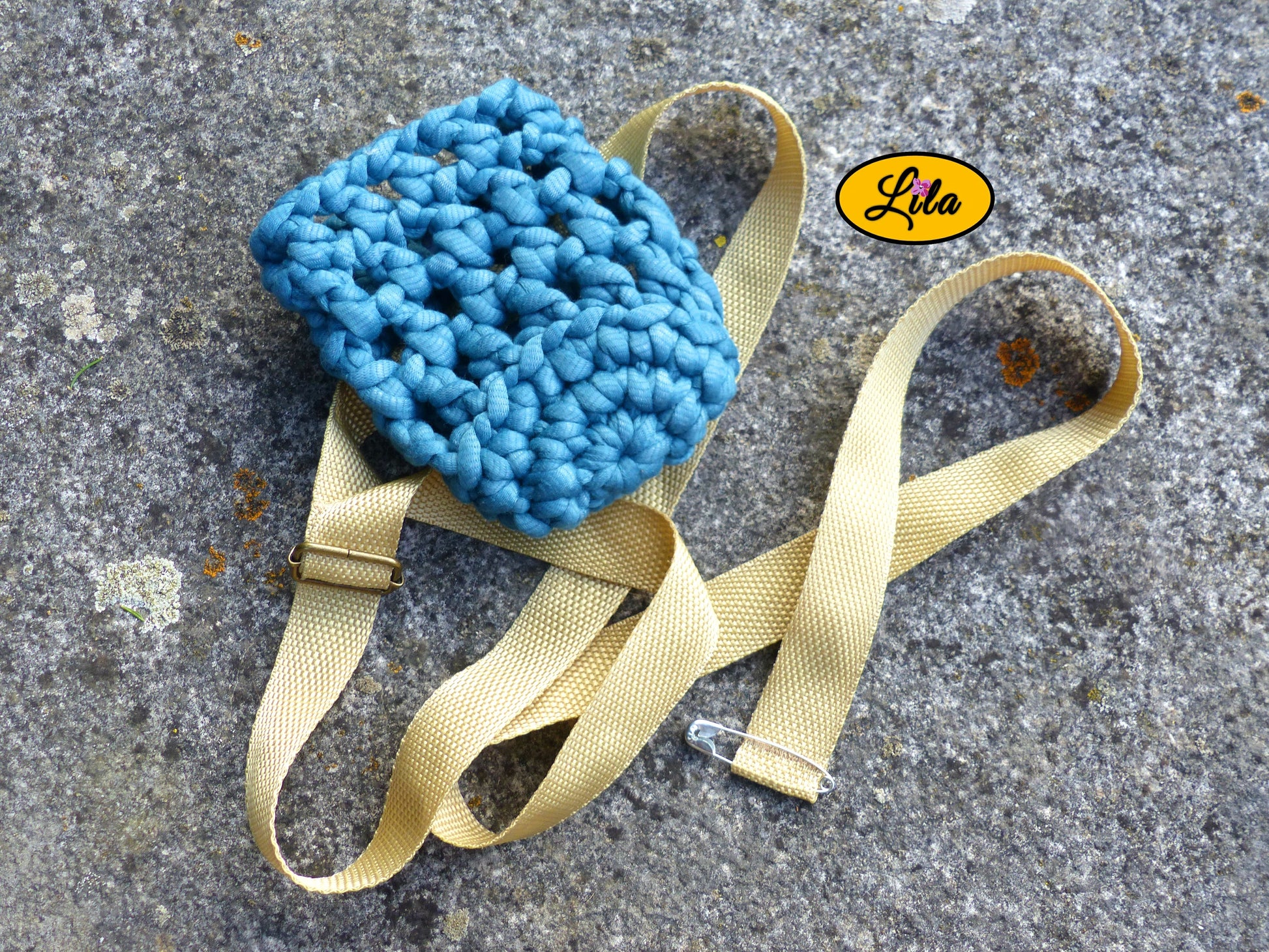 Porte-gobelet en laine turquoise vu de haut sans gobelet posé sur une pierre avec ceinture couleur sable placée vers le bas style festival et artisanal