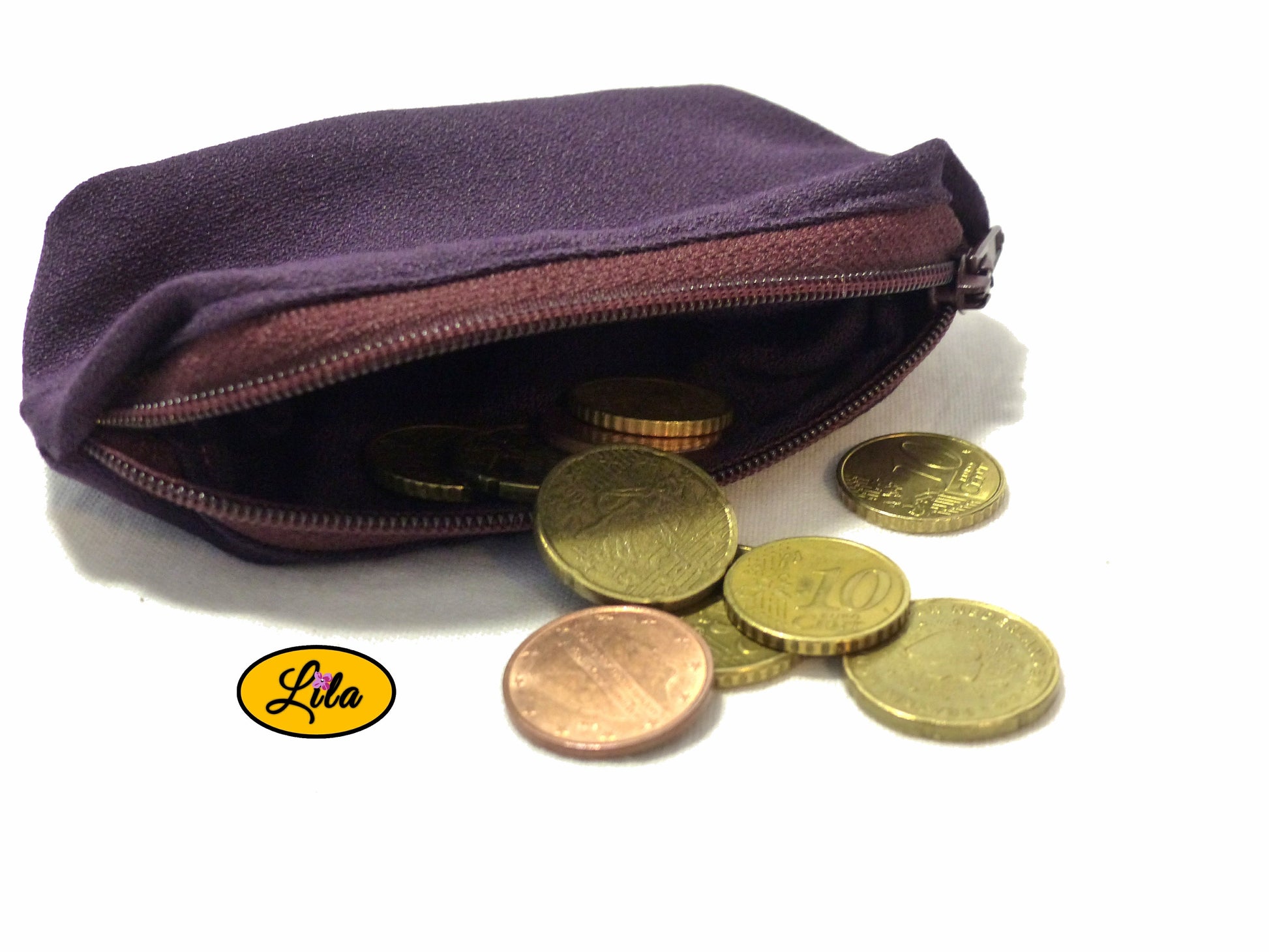 Porte-monnaie mauve avec fermeture éclair bordeaux ouvert avec pièces de monnaie qui en sortent sur fond blanc style artisanal et fonctionnel