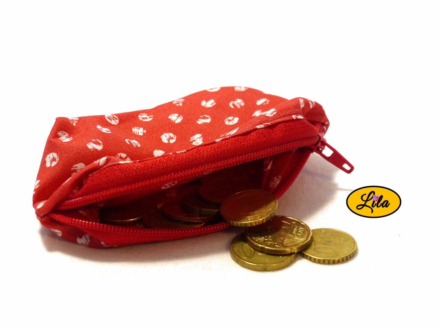 Porte-monnaie en tissu rouge à pois blancs ouvert avec pièces de monnaie qui en sortent sur fond blanc style artisanal et fonctionnel
