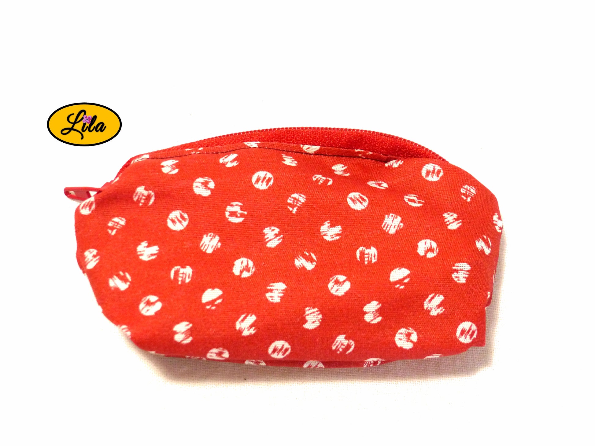 Porte-monnaie en tissu rouge à pois blancs avec fermeture éclair rouge posé de face vue de haut sur fond blanc style rétro et artisanal