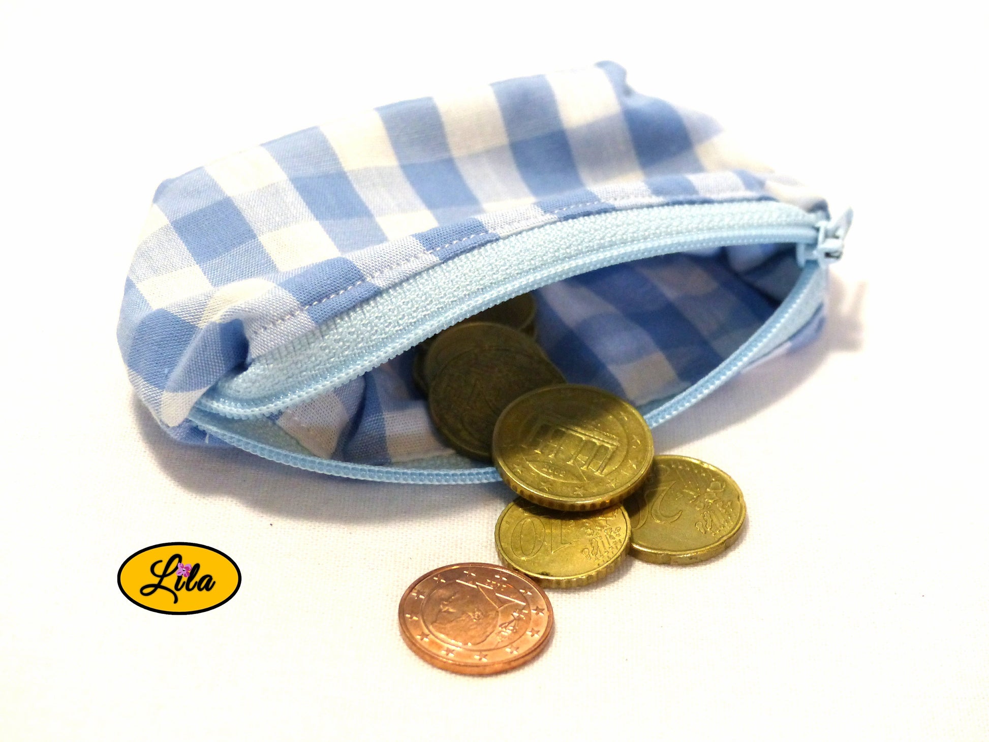 Porte-monnaie en tissu vichy bleu et blanc ouvert avec pièces de monnaie qui en sortent sur fond blanc style artisanal et fonctionnel