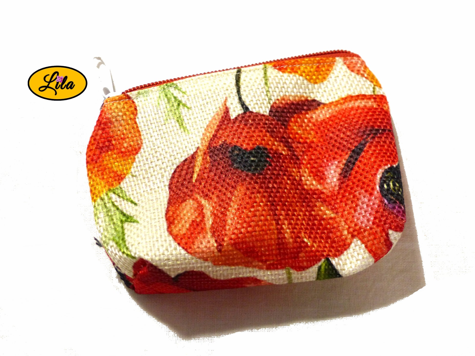Porte-monnaie en tissu vintage à motifs coquelicots issu d’une ancienne nappe avec fermeture éclair rouge et blanche posé de face vue de haut sur fond blanc style rétro et artisanal