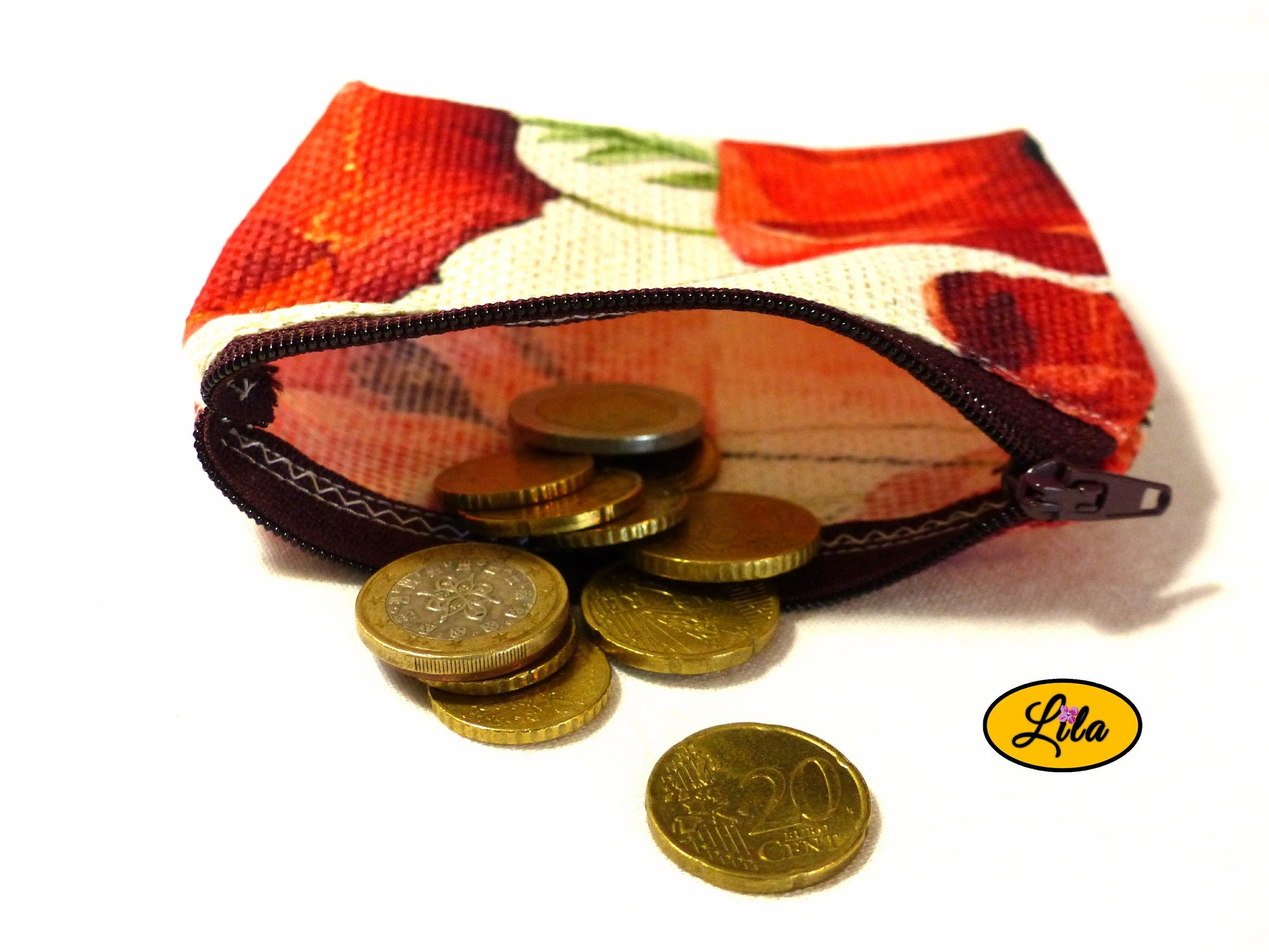 Porte-monnaie en tissu vintage à motifs coquelicots ouvert avec pièces de monnaie qui en sortent sur fond blanc style artisanal et fonctionnel