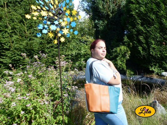Sac 4 saisons en simili cuir brun et turquoise porté à l’épaule par une femme devant un étang style élégant et tendance