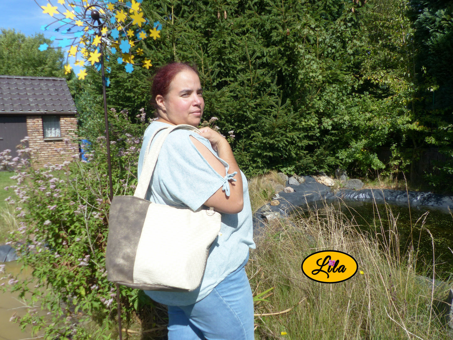Sac 4 saisons en simili cuir crème texturé et brun doré porté à l’épaule par une femme en jeans et haut vert devant un étang style chic quotidien