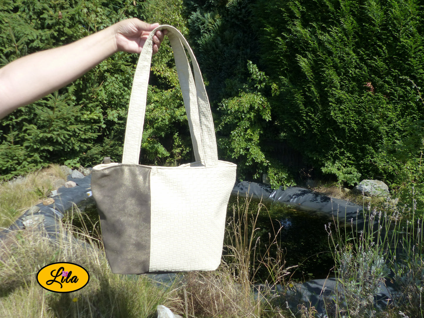 Sac 4 saisons en simili cuir blanc crème texturé et brun doré porté à la main devant un jardin et un étang style élégant et naturel
