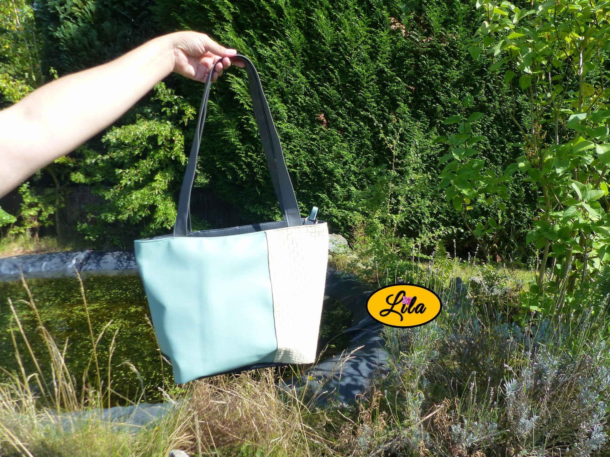 Sac 4 saisons en simili cuir crème texturé et vert porté à la main devant un jardin et un étang style élégant et naturel