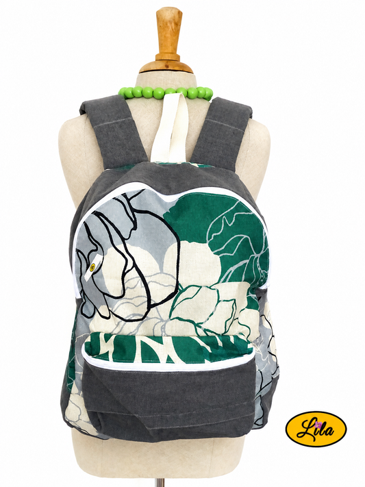 Sac à dos artisanal en tissu gris et tissu floral graphique vert, gris et écru présenté sur mannequin de couture sur fond blanc avec poche zippée sur le devant, bretelles en sangle crème et porte-bouteilles latéraux