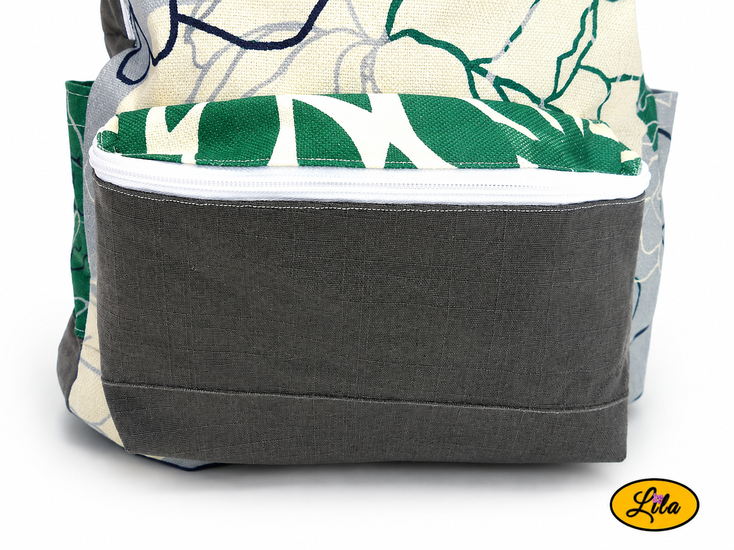 Zoom sur la poche avant zippée d’un sac à dos en tissu gris et motifs floraux graphiques verts, gris et écru style artisanal et fonctionnel