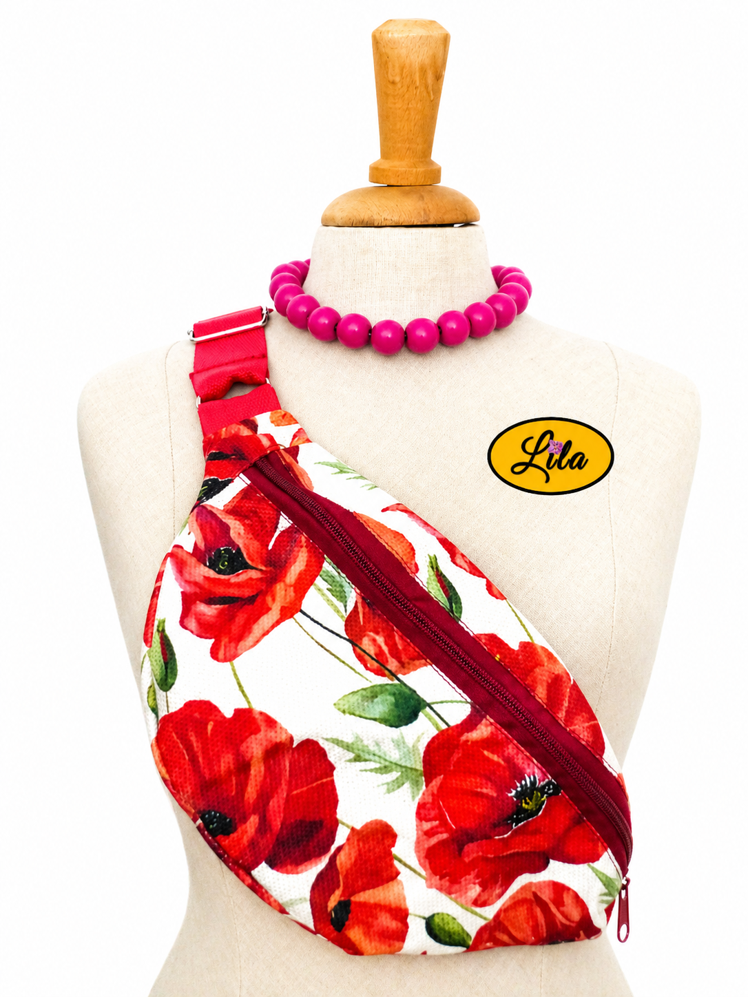 Sac banane vintage aux motifs de coquelicots avec sangle rouge et fermeture éclair bordeaux porté sur mannequin de couture sur fond blanc style bohème et artisanal