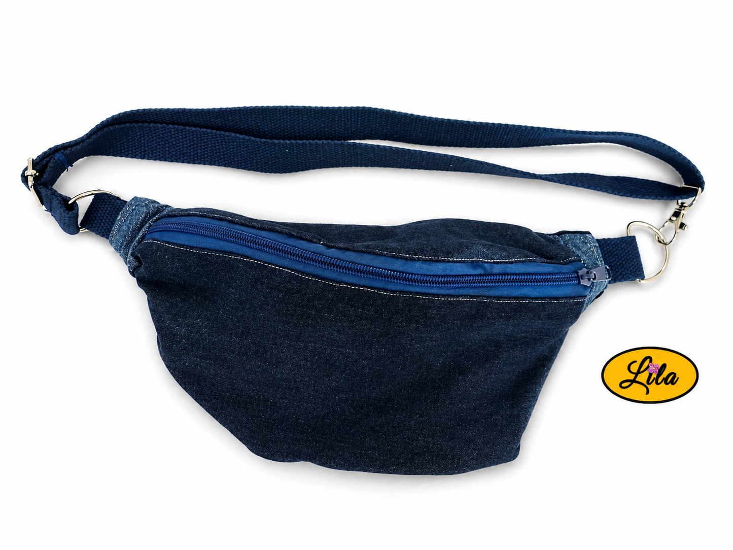 Sac banane en jeans foncé avec fermeture éclair bleu foncé et sangle bleu foncé posé à plat vue de face avec sangle sur le dessus sur fond blanc style casual et artisanal