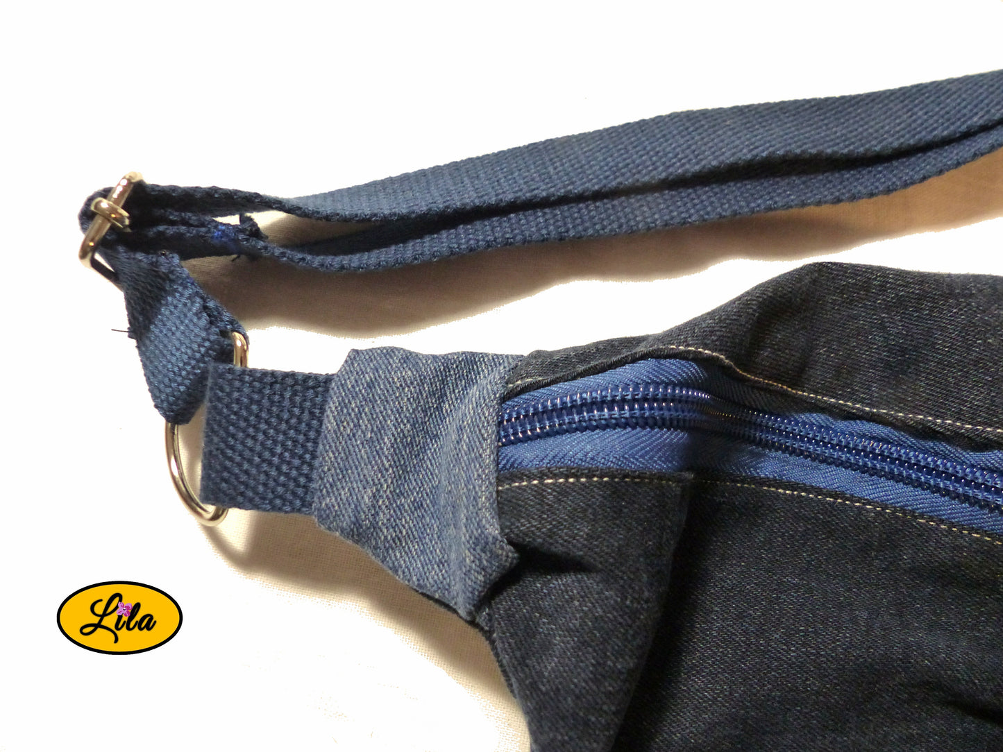 Zoom sur le coin du sac banane en jeans recyclés où la sangle bleue en coton est attachée détail couture et finition artisanale