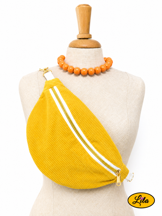 Sac banane en velours côtelé jaune avec sangle blanche fermeture éclair blanche et tirette dorée porté sur mannequin de couture sur fond blanc style tendance et vintage