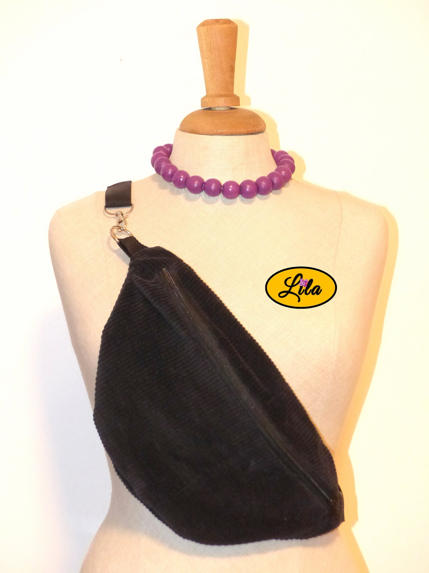 Sac banane en velours côtelé noir avec sangle noire et fermeture éclair noire porté sur mannequin de couture sur fond blanc style chic et moderne