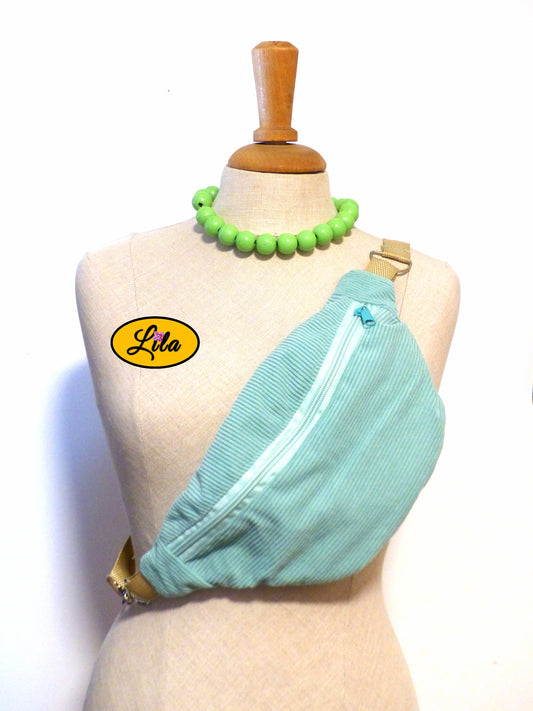 Sac banane en velours côtelé vert menthe avec sangle assortie et anse couleur sable porté sur mannequin de couture sur fond blanc style cocooning et urbain