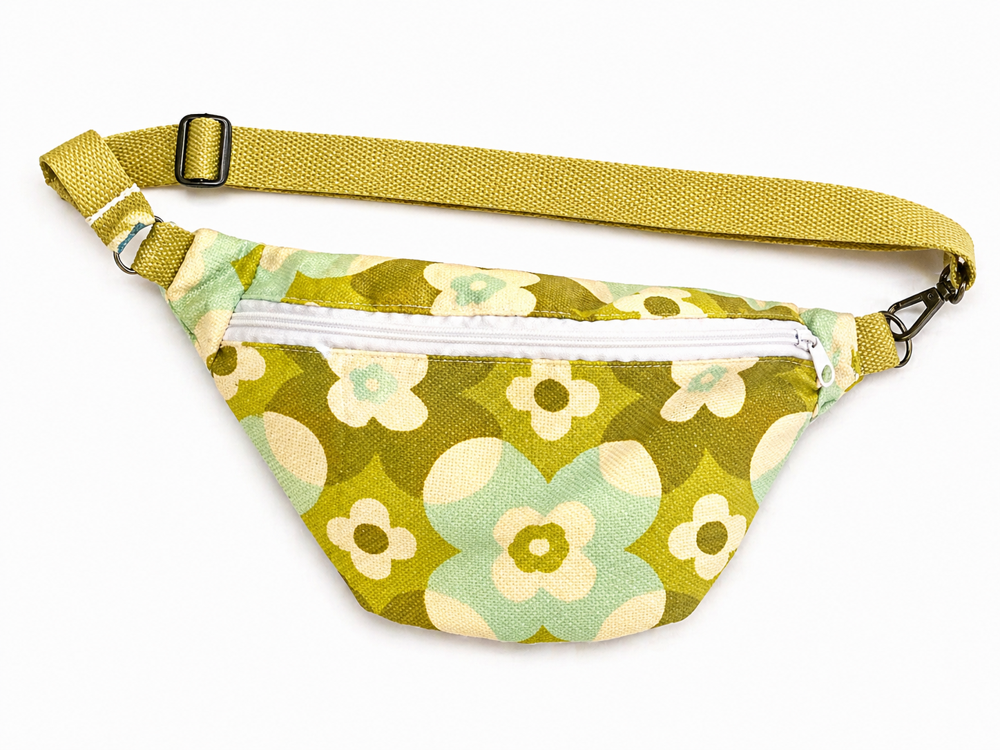 Sac banane vintage fleurie verte avec sangle kaki et fermeture éclair blanche posé à plat vue de face avec sangle au-dessus sur fond blanc style rétro et tendance