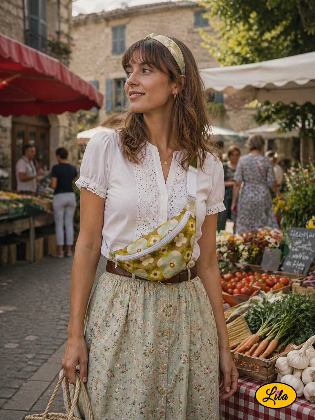 Sac banane en tissu vintage vert fleuri avec fermeture éclair grise et sangle grise porté par une jeune fille en chemisier à dentelle et longue jupe à petites fleurs avec bandeau vert fleuri dans les cheveux devant un stand de fruits et légumes style bohème et champêtre