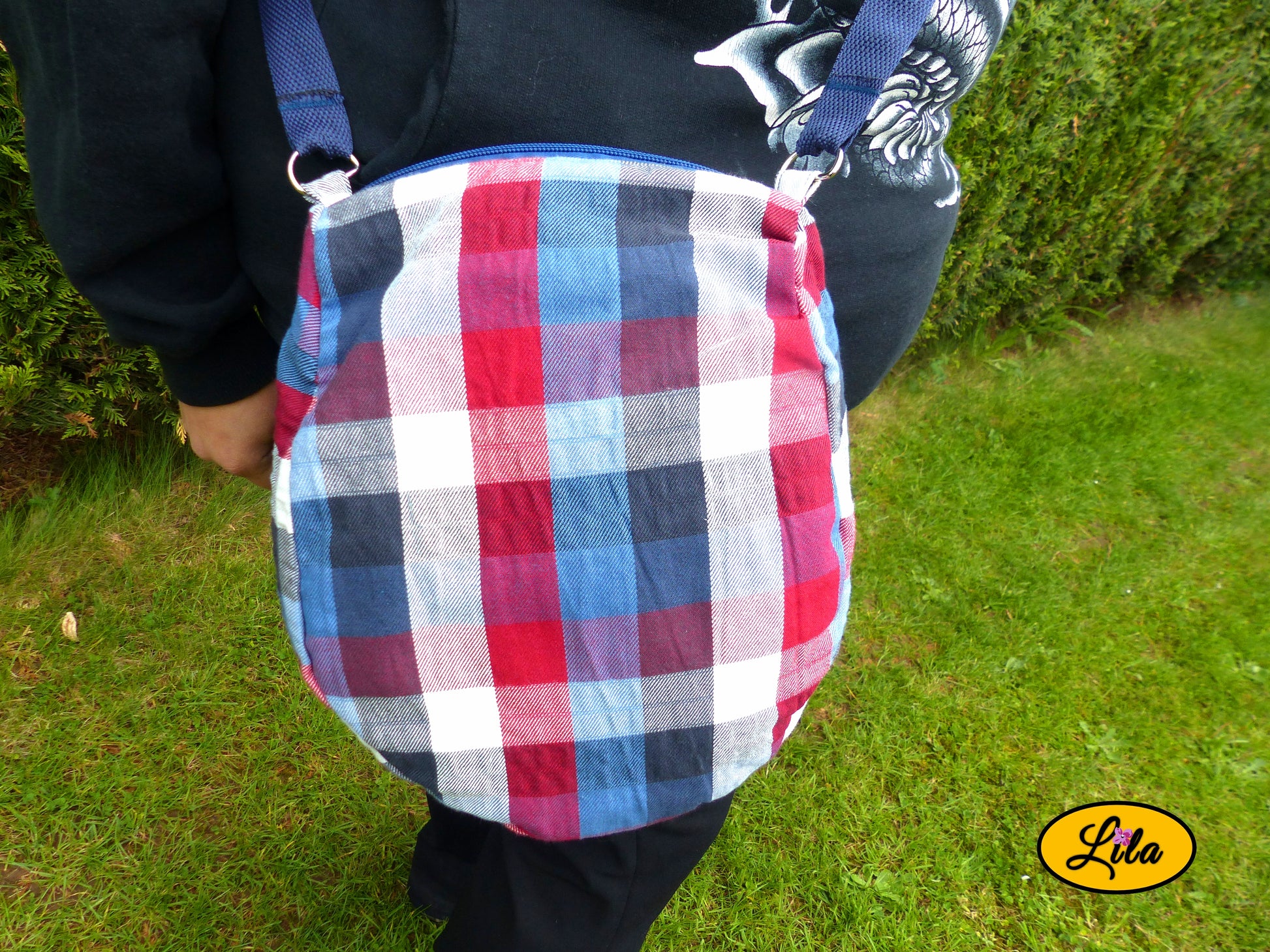 Sac bandoulière en tartan bleu blanc rouge porté en extérieur cadré sur la taille pour montrer le rendu porté style urbain et moderne