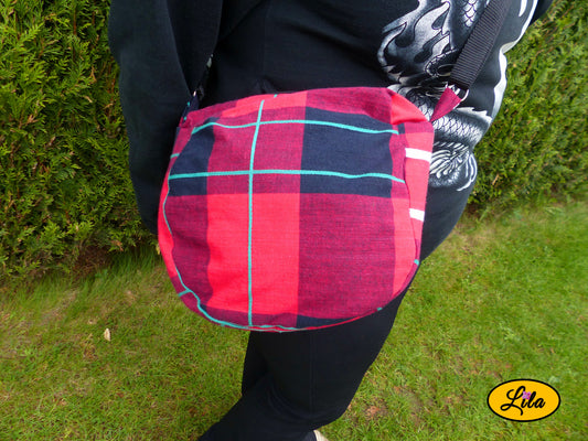 Sac bandoulière en tartan rouge porté en extérieur cadré sur la taille style urbain et tendance