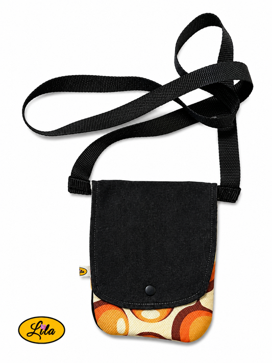 Sac bandoulière pour téléphone en jeans noir avec rabat en tissu vintage à motifs de ronds orange vu de haut sur fond blanc, fermeture à pression blanche et sangle en coton blanc, création artisanale