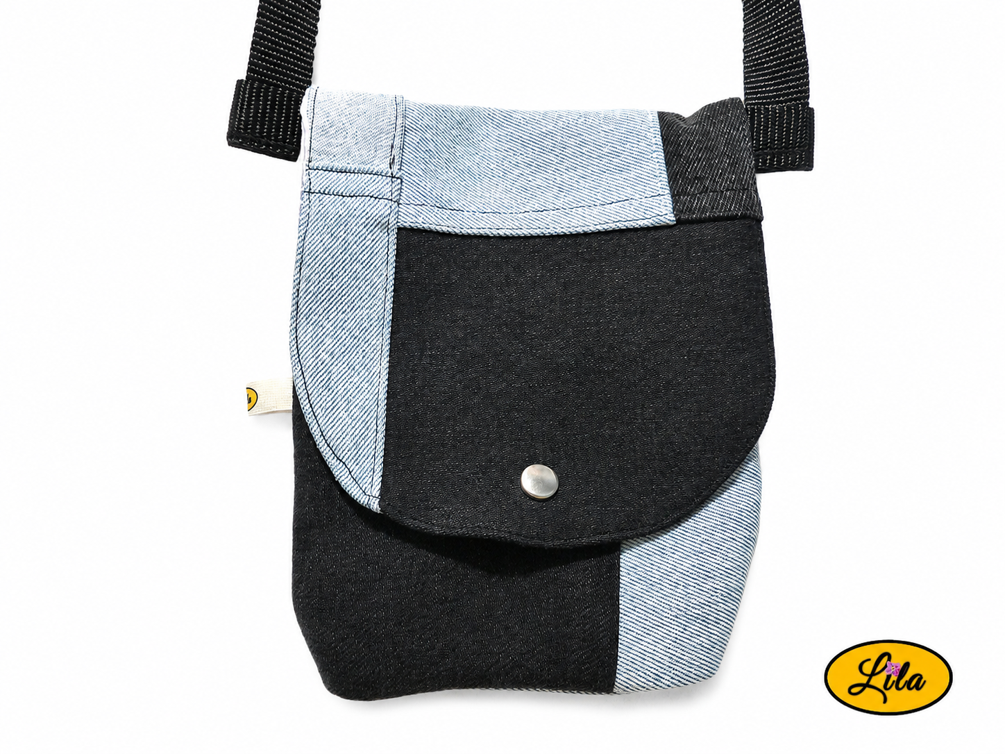 Zoom sur un sac bandoulière pour téléphone en patchwork de jeans bleu clair et noir fermé sans les sangles sur fond blanc mettant en valeur l'assemblage des tissus recyclés et la fermeture à pression argentée
