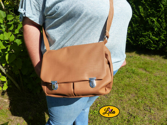 Sac besace en simili cuir brun légèrement craquelé porté en bandoulière par une femme avec bras dans le dos photo cadrée sur le sac style chic et vintage