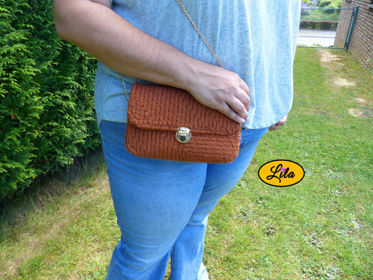 Sac en laine brun pailleté sur canevas rigide porté par un mannequin légèrement de profil en extérieur avec la main posée sur le sac style chic et tendance