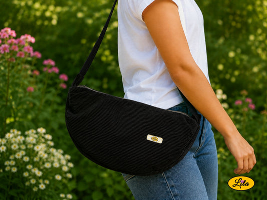 Sac Luna noir en velours côtelé porté à l’épaule par un mannequin en jeans et t-shirt en extérieur photo cadrée sur le sac style urbain et tendance