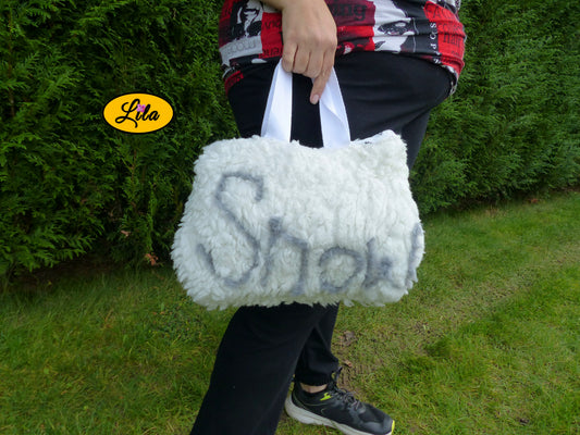 Sac à main en fausse fourrure blanche avec inscription SNOW en laine grise porté à la main en extérieur photo cadrée sur le sac style hivernal et cocooning