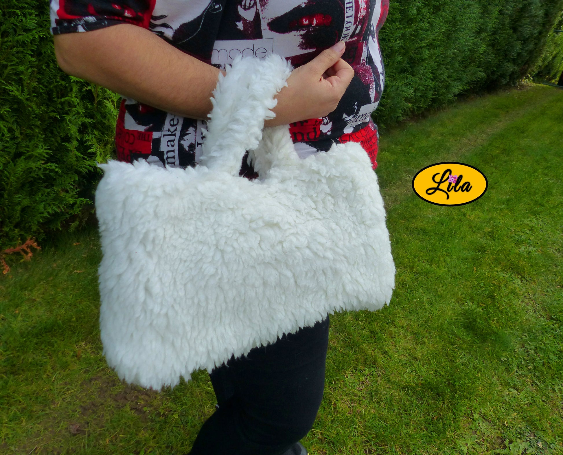 Sac à main entièrement en fausse fourrure blanche porté au creux du poignet par une mannequin en extérieur photo cadrée sur le sac style chic et cocooning