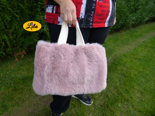 Sac à main en fausse fourrure vieux rose avec anse en coton blanc crème porté à la main par un mannequin en extérieur photo cadrée sur le sac style chic et cocooning