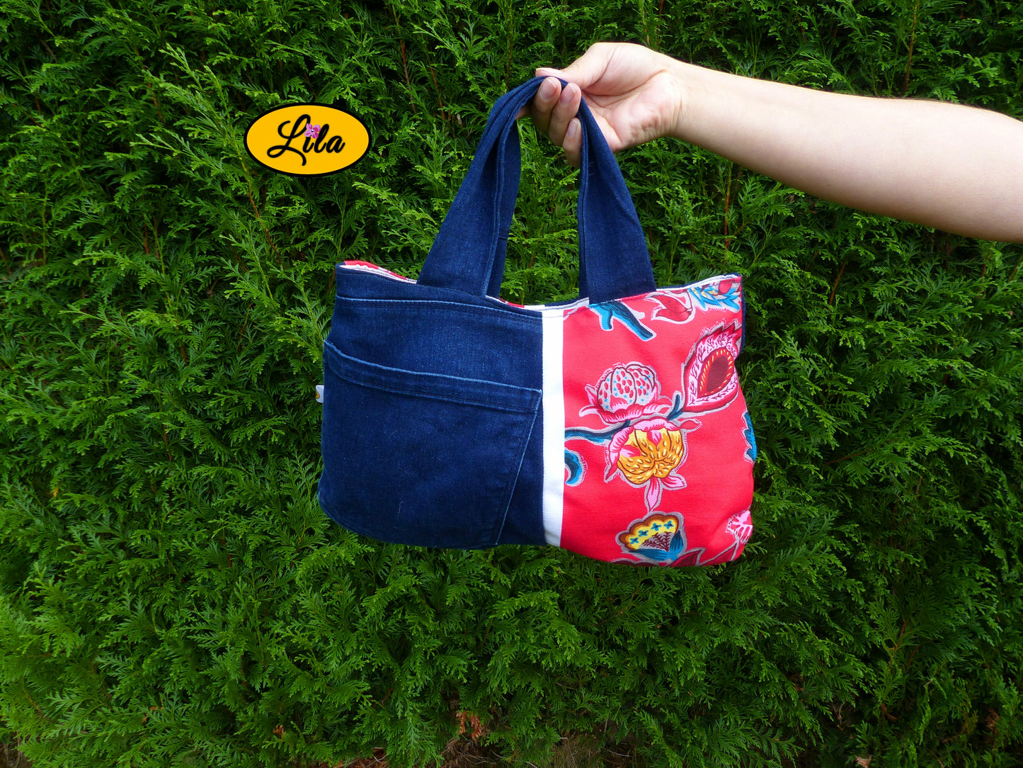 Sac à main en jeans et tissu floral rose porté à bout de bras devant une haie style naturel et romantique