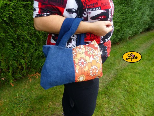 Sac à main en jeans et ancienne nappe vintage orange fleurie porté dans le creux du bras en extérieur photo cadrée sur le sac style rétro et artisanal