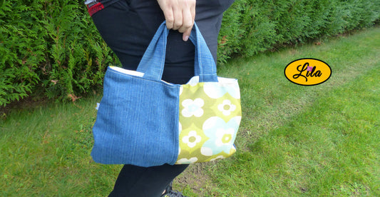 Sac à main en jeans et ancienne nappe vintage verte fleurie porté à la main en extérieur photo cadrée sur le sac style bohème et artisanal