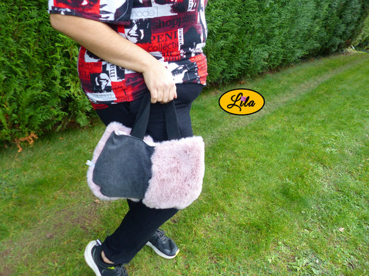 Sac à main en jeans noir et fausse fourrure vieux rose porté à la main en extérieur photo cadrée sur le sac style chic et hivernal