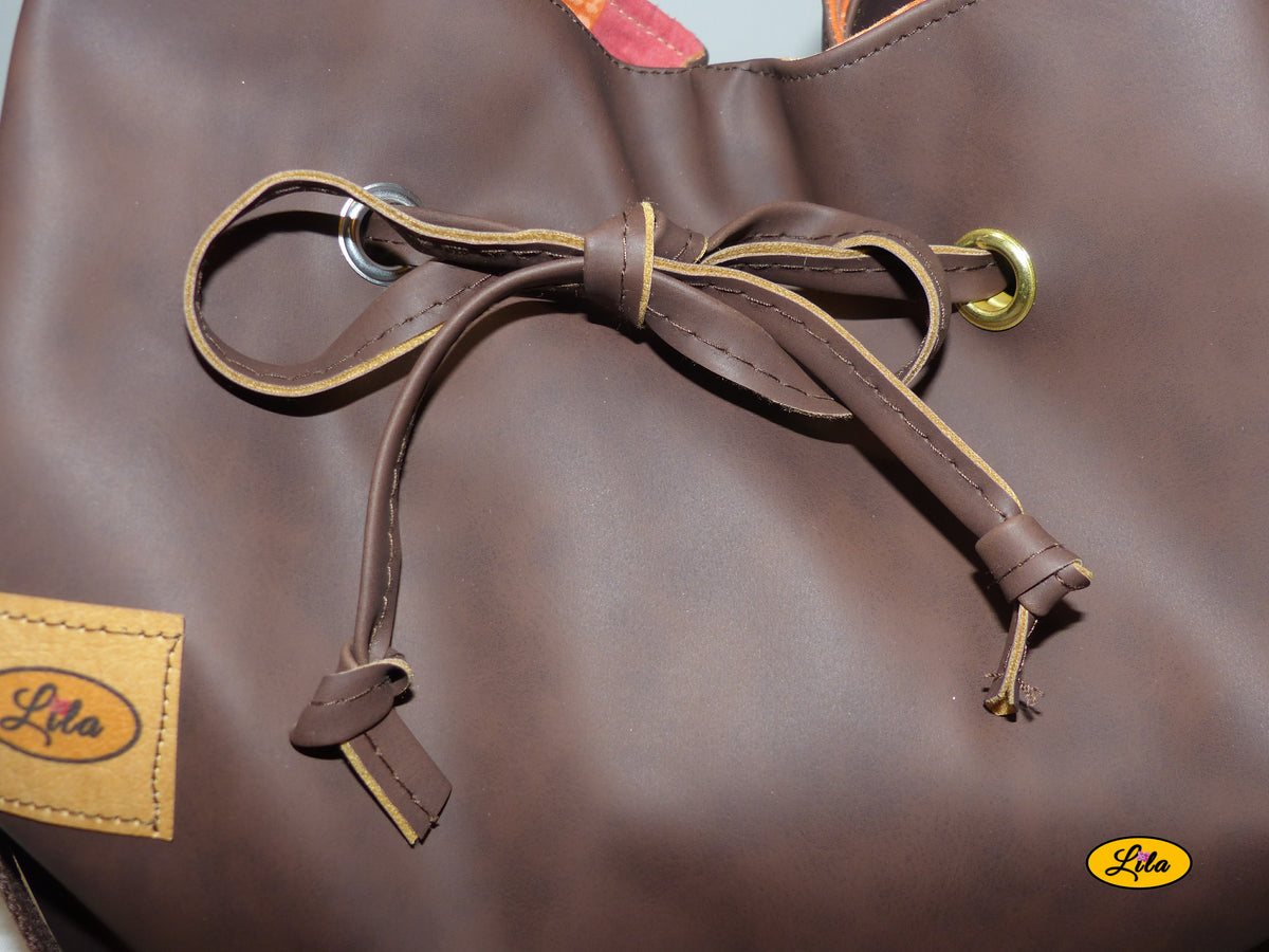 Zoom sur le lien coulissant noué sur le devant d'un sac seau en simili cuir brun foncé, détail de fermeture et finition artisanale