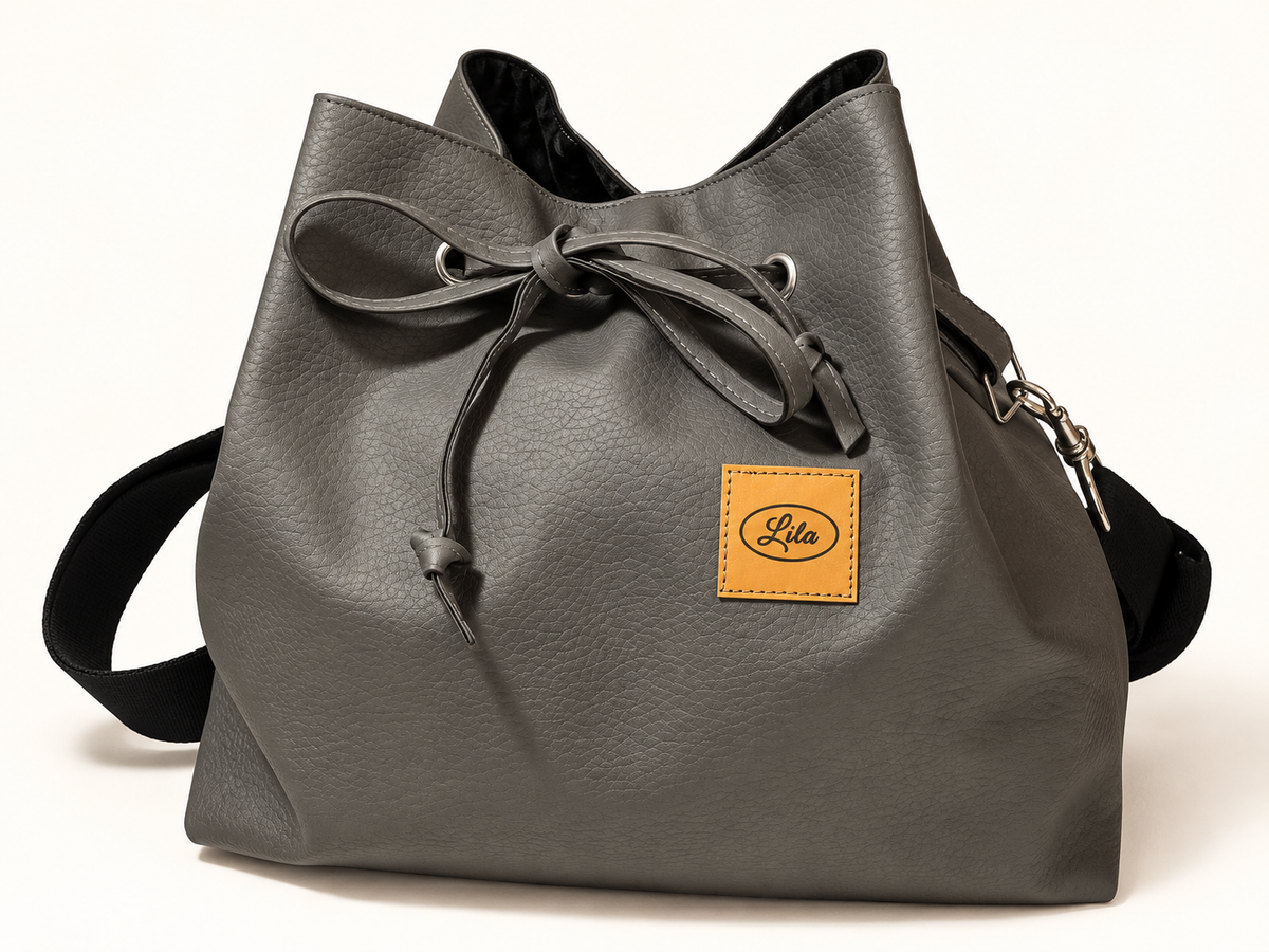 Sac seau en simili cuir gris vu de face sur fond blanc avec sangle noire récupérée placée derrière le sac et lien coulissant visible
