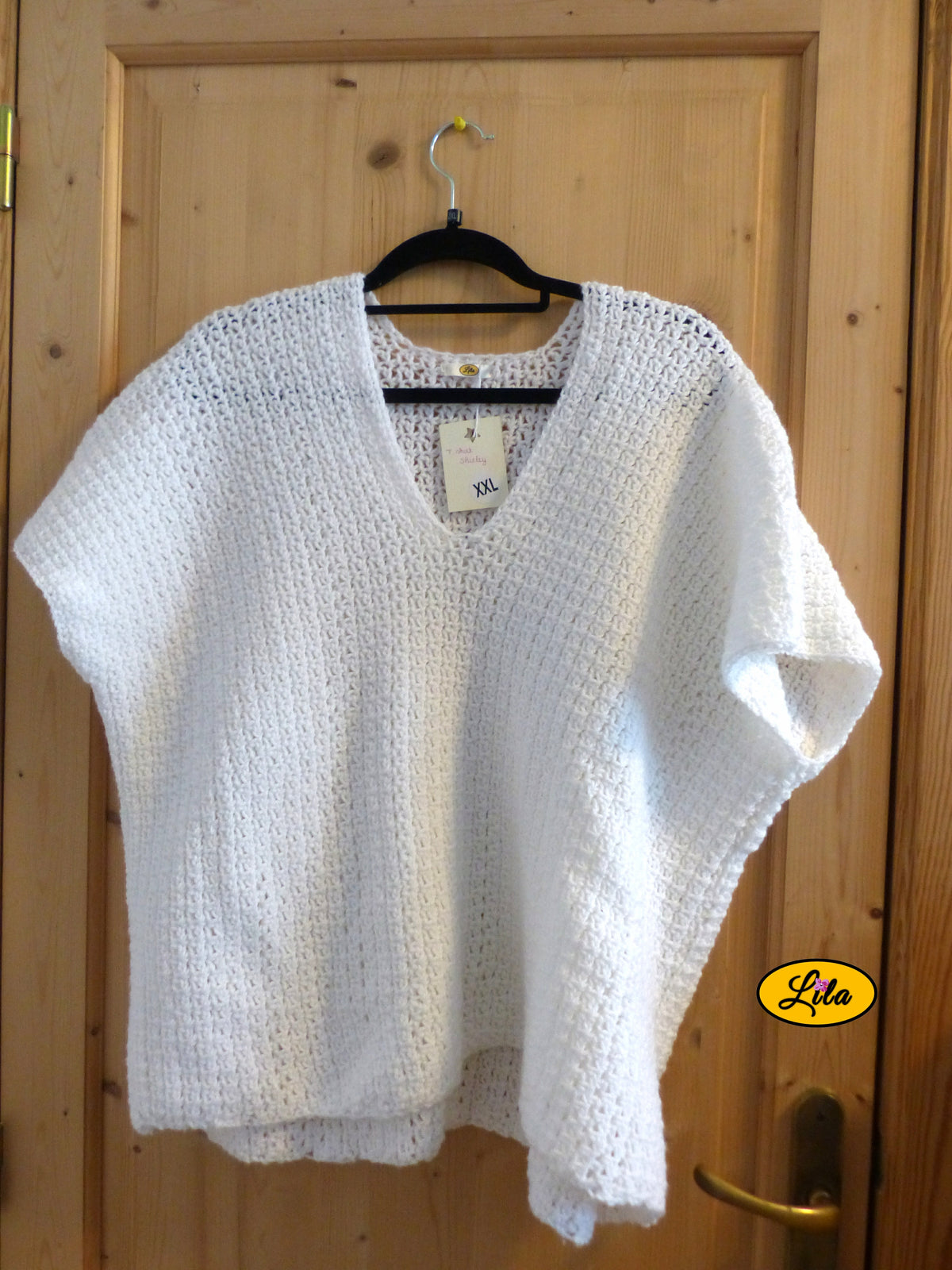 T-shirt blanc crocheté à la main en laine acrylique, taille 2XL, présenté sur cintre accroché à une porte, vue de face