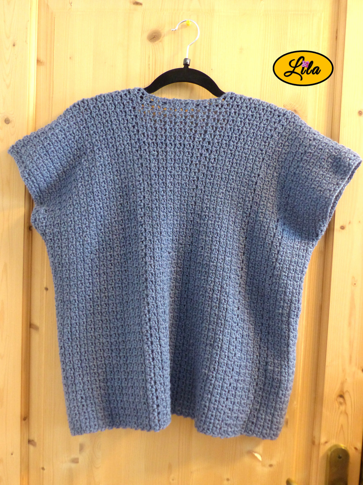 T-shirt bleu crocheté à la main en laine acrylique, taille M, présenté sur cintre accroché à une porte, vue de dos