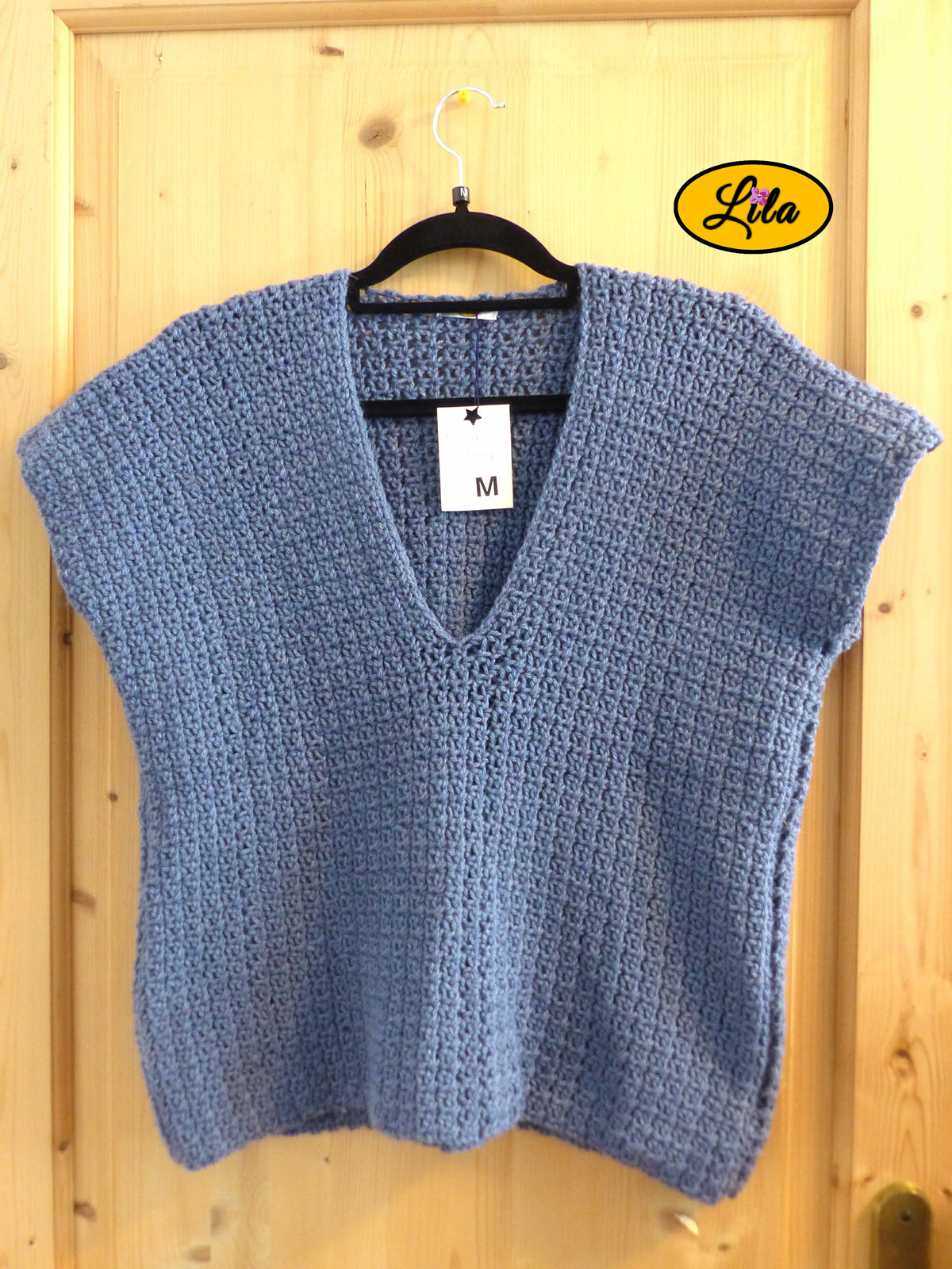 T-shirt bleu crocheté à la main en laine acrylique, taille M, présenté sur cintre accroché à une porte, vue de face